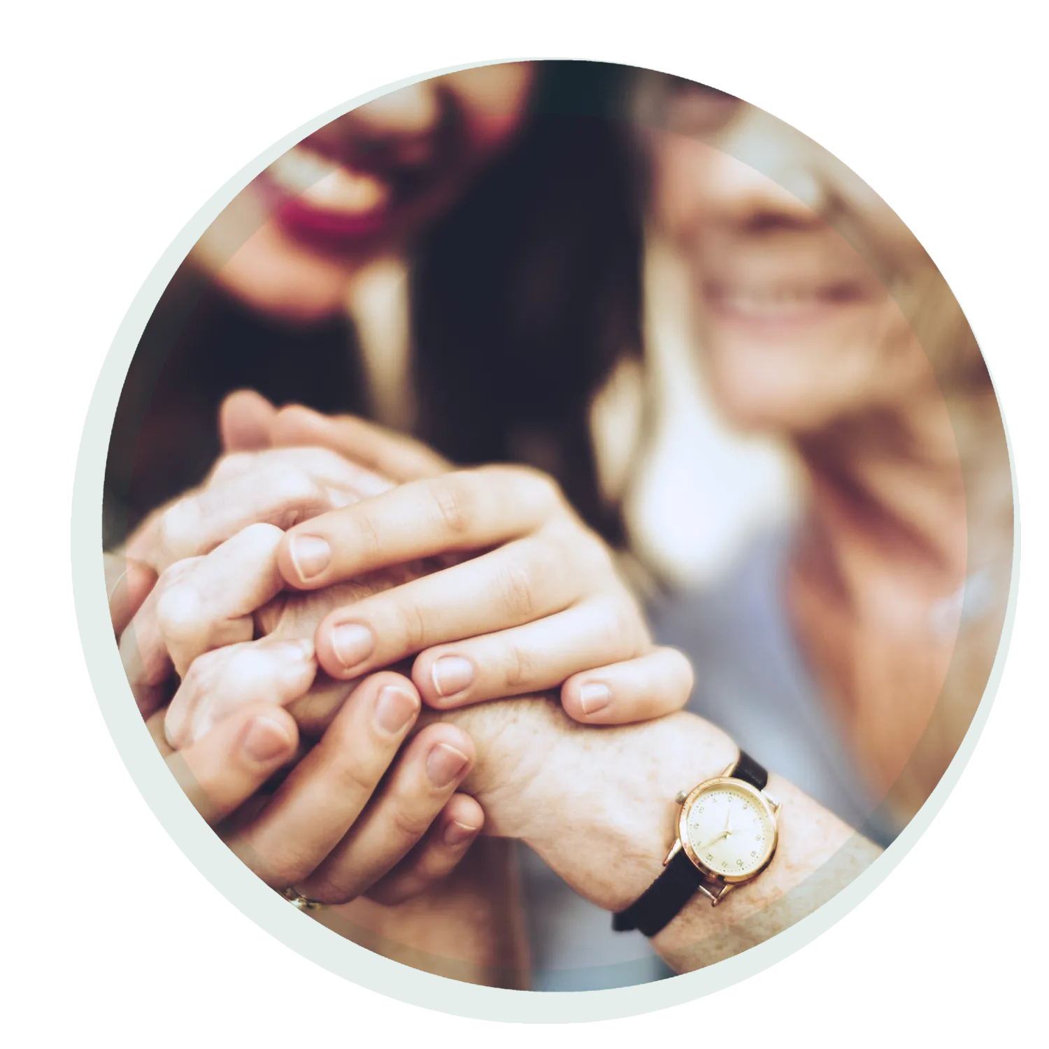 Nahaufnahme von zwei sich haltenden Händen. Die jüngere Hand umfasst sanft die ältere Hand einer Person. Beide Personen lächeln, aber sind unscharf dargestellt. Die ältere Person trägt eine Uhr.
